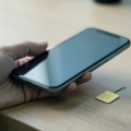 A hand holding a smartphone showing a SIM settings screen next to a small physical SIM card on a desk