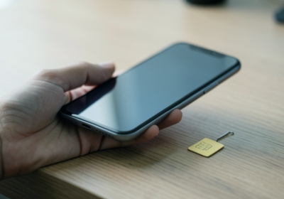 A hand holding a smartphone showing a SIM settings screen next to a small physical SIM card on a desk