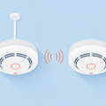 Flat illustration of two ceiling smoke alarms, one wired and one linked by wireless signal arcs