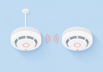 Flat illustration of two ceiling smoke alarms, one wired and one linked by wireless signal arcs