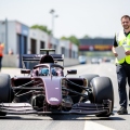 Formula 1-style car in the pit lane beside a race official in a high-visibility vest