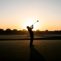 Lone golfer silhouette teeing off at dawn on an empty course