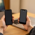 A person holding a new smartphone next to an older phone, setting up security codes at a desk