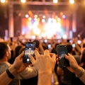 Concertgoers holding up phones at a venue entrance with stage lights glowing in the background