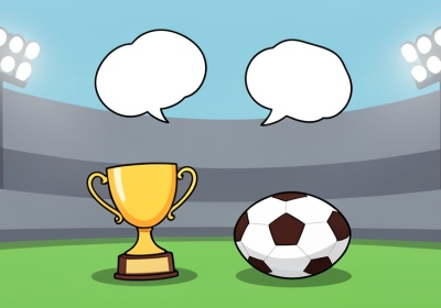 A small man-of-the-match trophy beside a football on grass under stadium lights