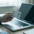 A person holding a credit card while reviewing account details on a laptop at a desk