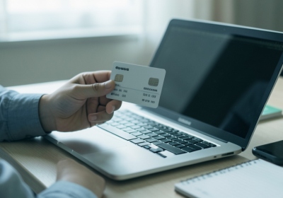 A person holding a credit card while reviewing account details on a laptop at a desk