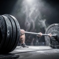 Chalked hands gripping a heavily loaded barbell under stacked plates on an arena stage