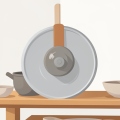 A potter's wheel with grey clay and simple unglazed ceramic bowls on a wooden shelf in a studio