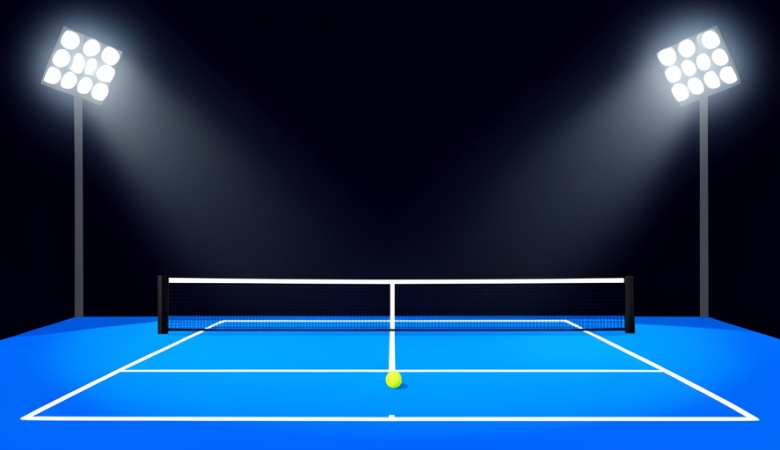 An empty blue tennis court at night under bright stadium floodlights with a single ball near the baseline