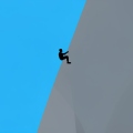 A small silhouette of a rock climber high on a tall vertical granite cliff against a blue sky